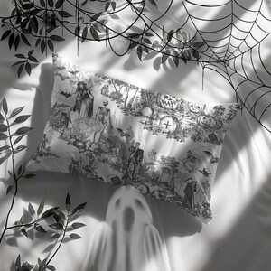 May include: A white pillowcase with a black and white Halloween-themed print featuring a witch, a skeleton, pumpkins, and a cross. The print is reminiscent of a vintage toile pattern.