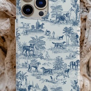 Op de afbeelding: Een witte iPhone-hoes met een blauw-wit toile-patroon met honden, bomen en andere natuur-ge&iuml;nspireerde ontwerpen.