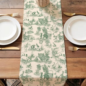 a table setting with a green and white table runner with a pattern of rabbits and other animals. There are two white plates and two gold forks arranged on the table.