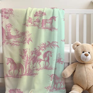 May include: A baby blanket featuring a pink unicorn toile design on a pale green and white backdrop. The blanket is draped over a white cot, with a teddy bear beside it.