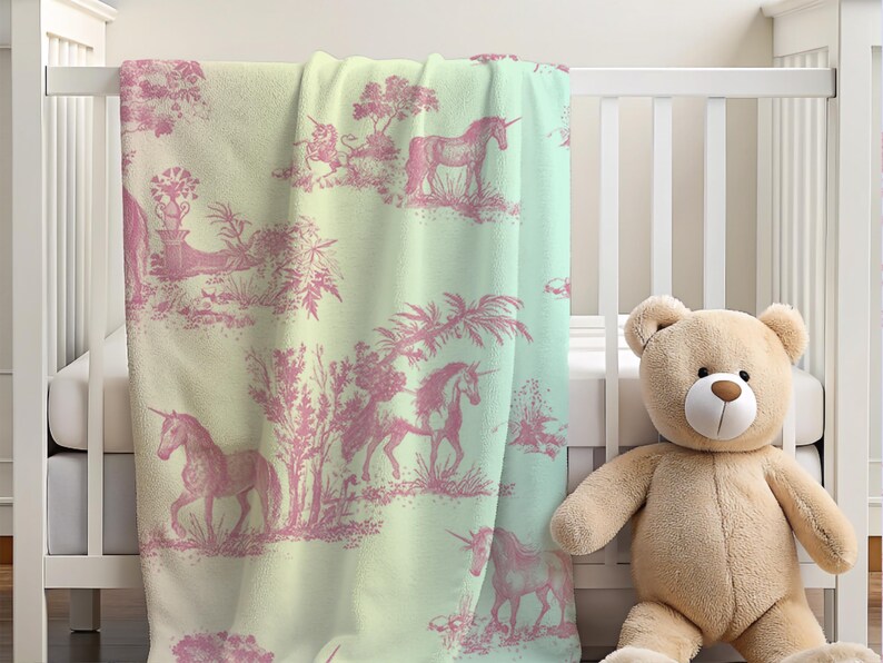 May include: A baby blanket featuring a pink unicorn toile design on a pale green and white backdrop. The blanket is draped over a white cot, with a teddy bear beside it.