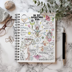 Peut inclure: Un carnet &agrave; spirales blanc pr&eacute;sentant une illustration d&eacute;taill&eacute;e avec le texte In My Spiritual Era. Le motif comprend une figure centrale en position du lotus, entour&eacute;e de divers symboles comme une fleur de lotus, une t&ecirc;te de Bouddha et du texte.
