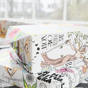 May include: Two gift boxes wrapped in white paper with colorful illustrations. The top box has the text "THE POWER OF NOW" and a drawing of a woman holding a sword. The bottom box has the text "IN MY SPIRITUAL ERA" and a drawing of a hand with a heart.