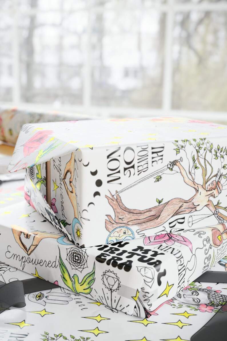 May include: Two gift boxes wrapped in white paper with colorful illustrations. The top box has the text "THE POWER OF NOW" and a drawing of a woman holding a sword. The bottom box has the text "IN MY SPIRITUAL ERA" and a drawing of a hand with a heart.