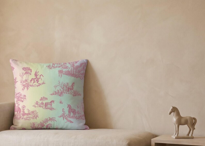 May include: A square cushion with a toile design depicting horses and riders in pink against a gradient background of yellow, green, and blue. The cushion is on a beige sofa.