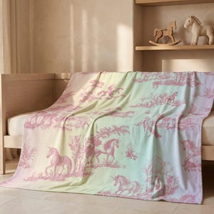 May include: A pastel-coloured blanket with a pink unicorn toile pattern draped over a wooden bed frame. The blanket features a gradient of colours, transitioning from pink to yellow and green. A wicker basket with stuffed animals sits nearby.