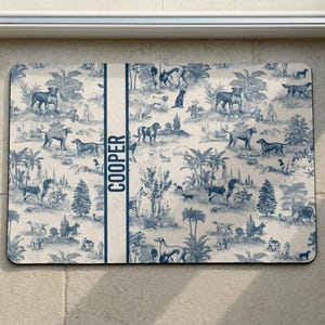 A decorative dog food mat with a repeating pattern of various animals and landscapes, including palm trees, birds, and other wildlife. The name "COOPER" is written in the center of the mouse pad.
