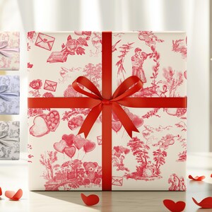 Pu&ograve; includere: Una scatola regalo bianca con un nastro e un fiocco rossi. La scatola &egrave; avvolta in carta con un motivo rosso e bianco di cuori, fiori e altri disegni romantici.