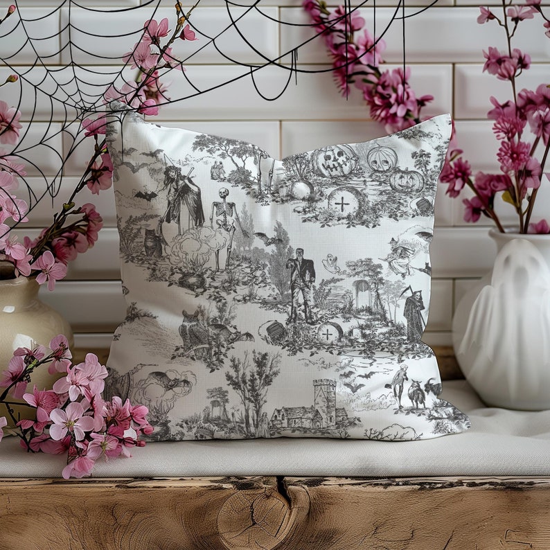 May include: A white throw pillow with a black and white Halloween-themed print. The print features skeletons, ghosts, bats, and pumpkins. The pillow is sitting on a wooden surface.