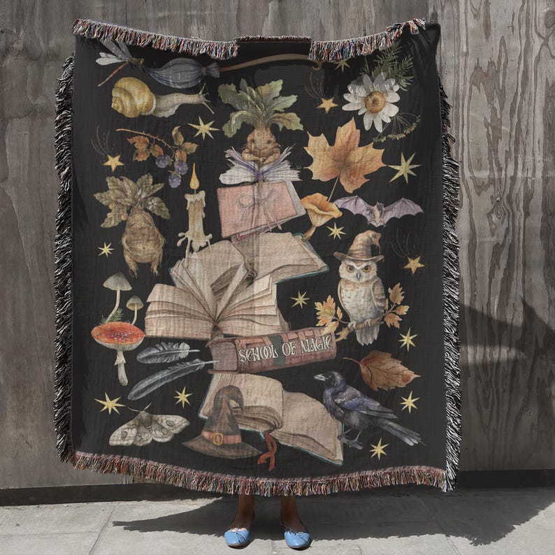 May include: A black woven tapestry throw blanket with a dark background and a variety of illustrations, including a book, an owl, a witch's hat, and the text "School of Magic".