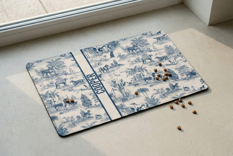A decorative dog bowl mat with a pattern of dogs and plants, placed on a white surface near a window.