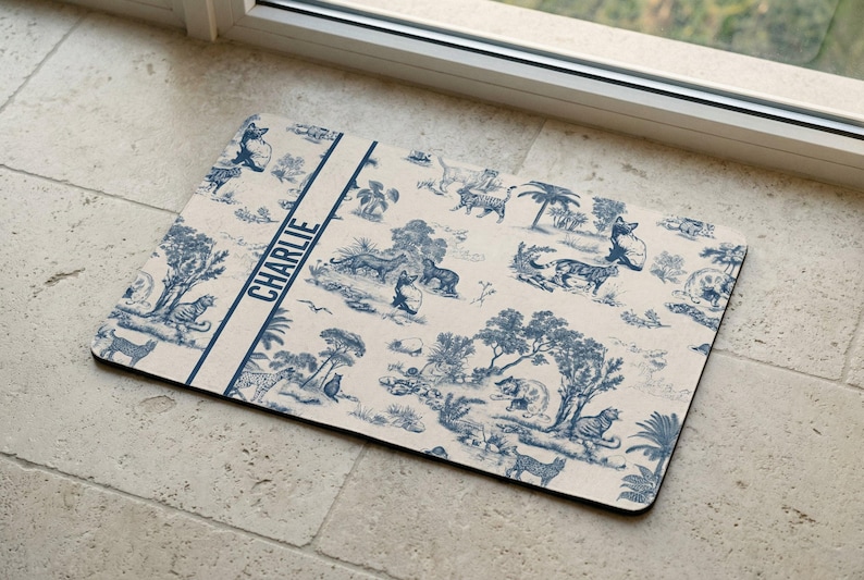 A decorative mat with a blue and white pattern featuring various animals and scenes, placed on a tiled floor near a window.