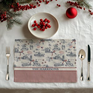 May include: A rectangular placemat with a patriotic design featuring illustrations of landmarks, fireworks, and flags in red, white, and blue. The bottom border has red and white stripes, with the text "THE HARRISONS" in the center.