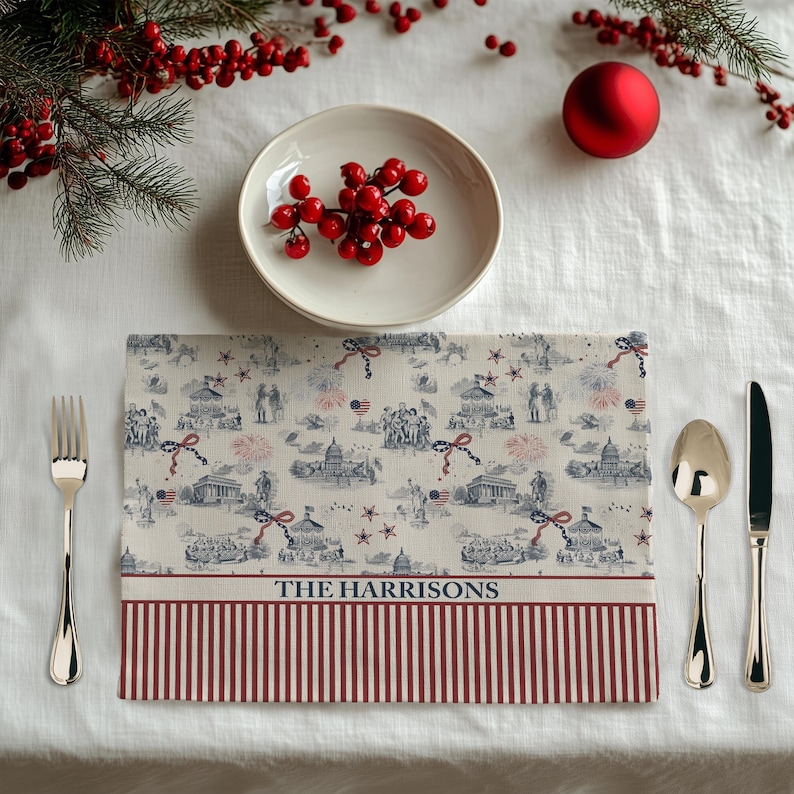 May include: A rectangular placemat with a patriotic design featuring illustrations of landmarks, fireworks, and flags in red, white, and blue. The bottom border has red and white stripes, with the text "THE HARRISONS" in the center.