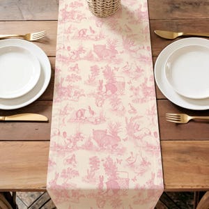 a table setting with a pink and white table runner featuring a pattern of rabbits and other animals. The table is set with white plates, forks, and knives, and the overall arrangement creates a visually appealing and harmonious dining experience.