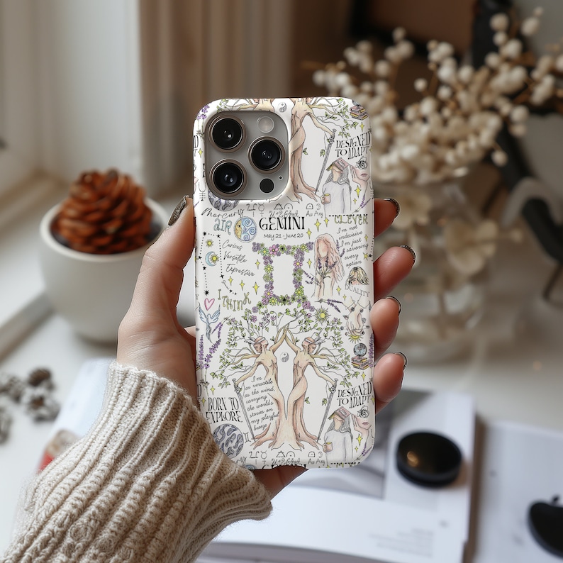 May include: A white phone case with a colorful illustration of the Gemini zodiac sign. The illustration includes a tree with two figures, flowers, and text that says "Gemini, May 21 - June 20, I'm clever, I'm adaptable, I'm curious, I'm a natural communicator, I'm a free spirit, I'm a dreamer, I'm a thinker, I'm a multitasker, I'm a social butterfly, I'm a lover of life, I'm a born to explore, I'm designed to disrupt".