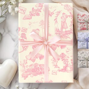 Pu&ograve; includere: Un regalo avvolto in carta a motivi rosa e bianchi con un nastro rosa. La carta presenta un motivo ripetitivo di cuori, palloncini e fiori. Tre scatole regalo pi&ugrave; piccole sono visibili sullo sfondo, avvolte in carta a motivi rosa, blu e grigi.