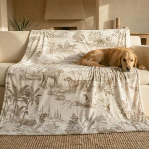 A golden retriever dog is resting on a couch with a blanket featuring a jungle scene design.