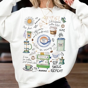 Könnte beinhalten: Weißes Sweatshirt mit einem farbenfrohen Kaffee-Themen-Design. Das Design zeigt Kaffeetassen, eine Kaffeemaschine und Texte wie "But first, coffee!" und "Sip, Smile, Repeat." Das Thema ist Kaffee und gute Laune.
