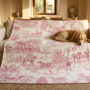 A golden retriever dog is resting on a pink and white patterned blanket on a beige couch in a cozy living room.