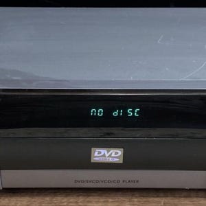Könnte beinhalten: Silberner AFREEY DVD-Player mit schwarzem Bedienfeld und digitaler Anzeige "NO DISC". Der Player hat eine Power-Taste, eine Play/Pause-Taste und eine Navigationstaste. Das DVD-Logo ist sichtbar.