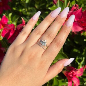 May include: A hand with white ombre nails wearing a silver turtle ring and a silver band ring.
