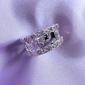 May include: A silver ring with a crown design and clear cubic zirconia stones.