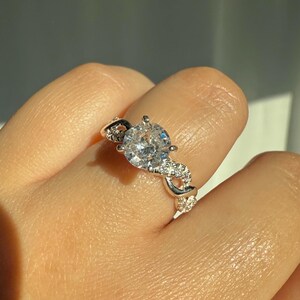 May include: A silver ring with a large, clear, round-cut gemstone surrounded by smaller, clear gemstones. The band is twisted and features a delicate design.