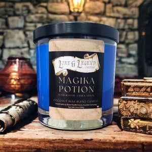 May include: A blue glass candle jar with a black lid. The label reads "LORE & LEGEND CANDLES" and "MAGIKA POTION POMEGRANATE CITRUS VIOLET COCONUT WAX BLEND CANDLE Handmade by Black Earth Creek Candle Company Net Wt: 8oz/226g".