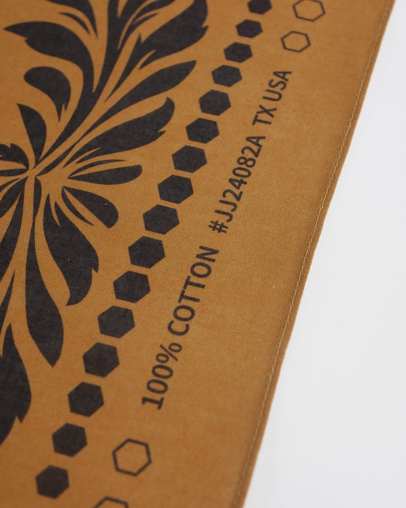 May include: Close-up of a brown fabric with a black floral design and a black border of hexagons. The fabric has the text "100% COTTON #JJ24082A TX USA" printed on it.