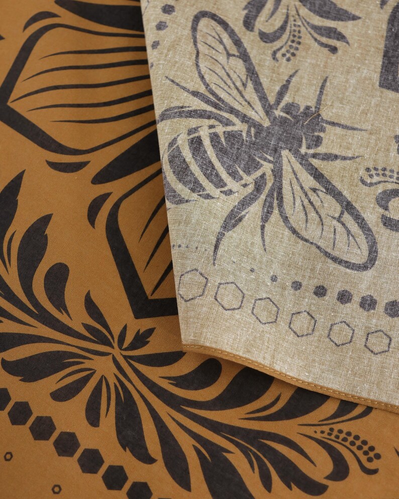 May include: A brown fabric with a black floral pattern and a honeycomb design. A beige fabric with a black bee design is layered on top.