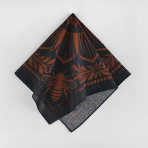 May include: A black bandana with a brown floral pattern and a bee design. The bandana has a fringe border and the text "100% Cotton" is printed on the bottom right corner.