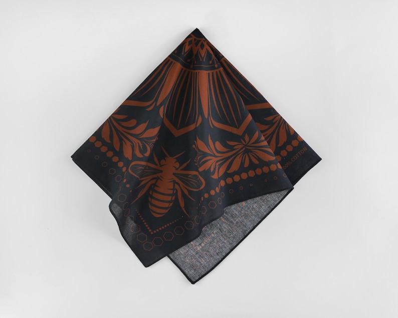 May include: A black bandana with a brown floral pattern and a bee design. The bandana has a fringe border and the text "100% Cotton" is printed on the bottom right corner.