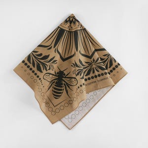 May include: A tan cotton bandana with a black bee and floral design. The bandana has a black border with the text "100% COTTON" and "STYLISH" printed on it.