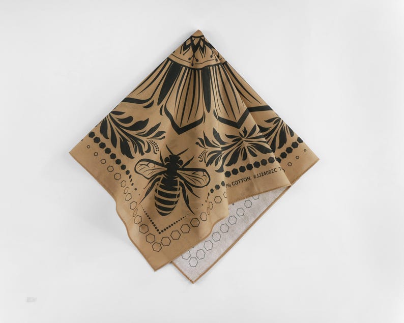 May include: A tan cotton bandana with a black bee and floral design. The bandana has a black border with the text "100% COTTON" and "STYLISH" printed on it.