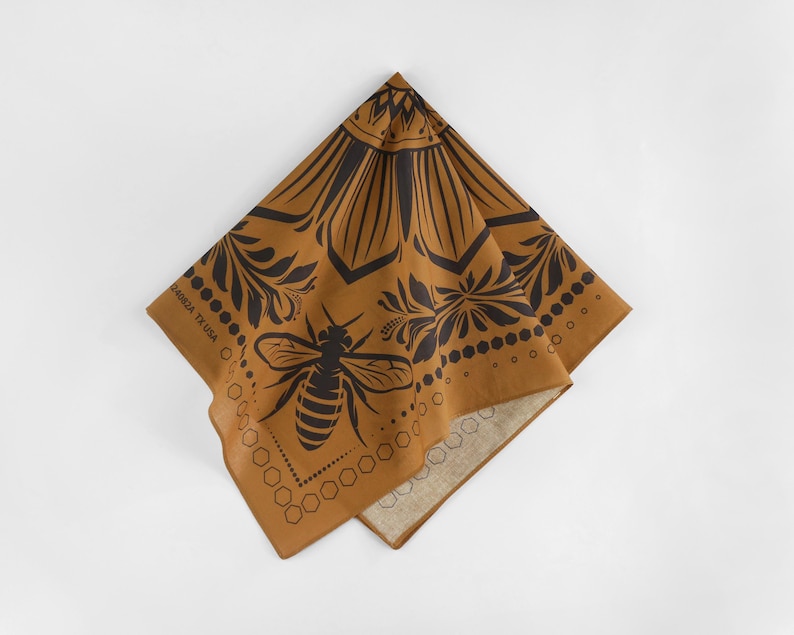 May include: A brown bandana with a black bee design and a floral pattern. The bandana has a white border and the text "HANDMADE TX USA" is printed on the border.