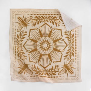 May include: A beige cotton bandana with a gold floral pattern and bee motifs. The bandana features a central mandala-like design with a repeating pattern of bees and flowers.