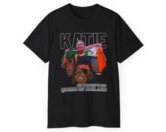 May include: Black t-shirt featuring a graphic of a female boxer holding championship belts. The text "KATIE 2X UNDISPUTED QUEEN OF IRELAND" is printed on the shirt.