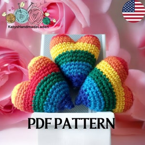 May include: Three crocheted rainbow hearts on a white surface. The hearts are made with red, orange, yellow, green, blue, and purple yarn. The text "PDF PATTERN" is printed below the hearts.