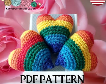 May include: Three crocheted rainbow hearts on a white surface. The hearts are made with red, orange, yellow, green, blue, and purple yarn. The text "PDF PATTERN" is printed below the hearts.