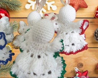 May include: Three crocheted angel ornaments with different colored trim. The angels are white with green, red, and blue trim. The ornaments are hanging from a wooden surface.