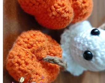 May include: Two crocheted orange pumpkins with brown stems and a white crocheted ghost with black eyes. The pumpkins and ghost are on a brown wooden surface. The text "PDF Pattern" is at the bottom of the image.