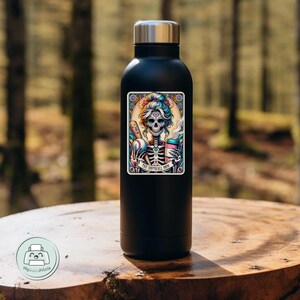 May include: Black stainless steel water bottle with a colorful sticker featuring a skeleton woman holding a baseball bat and a coffee cup. The sticker says "The Softball Mom".