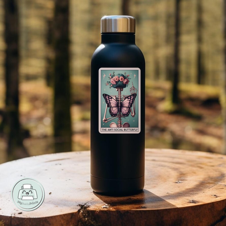 K&ouml;nnte beinhalten: Schwarze Edelstahl-Wasserflasche mit einem Aufkleber, der ein Skelett mit einem Schmetterling auf dem R&uuml;cken und einer Blumenkrone zeigt. Der Aufkleber lautet "The Anti Social Butterfly".