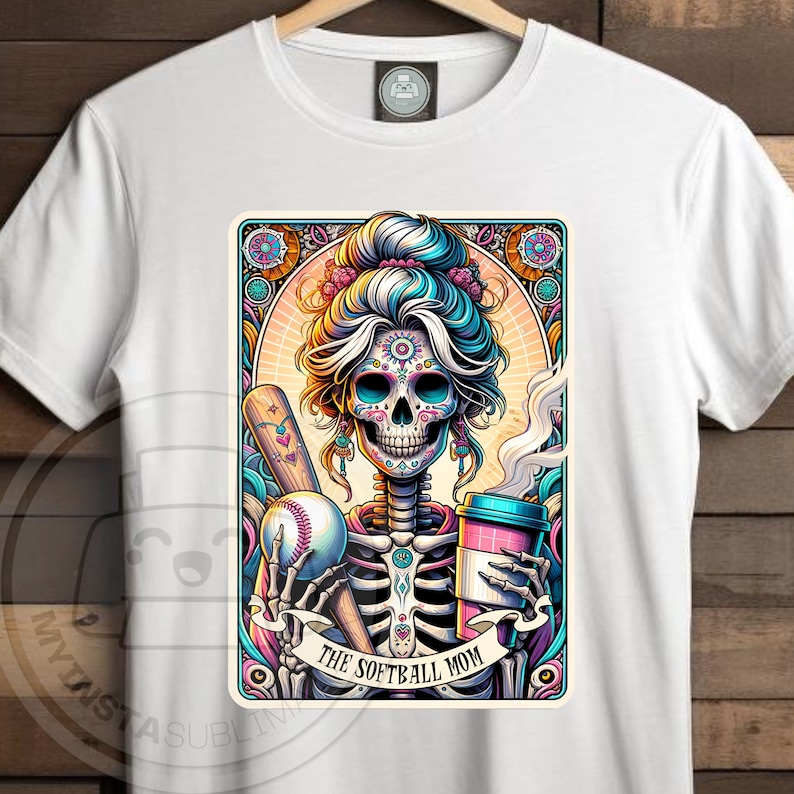 May include: A white t-shirt with a colorful illustration of a skeleton wearing a baseball cap and holding a bat and a cup of coffee. The text "The Softball Mom" is below the skeleton.