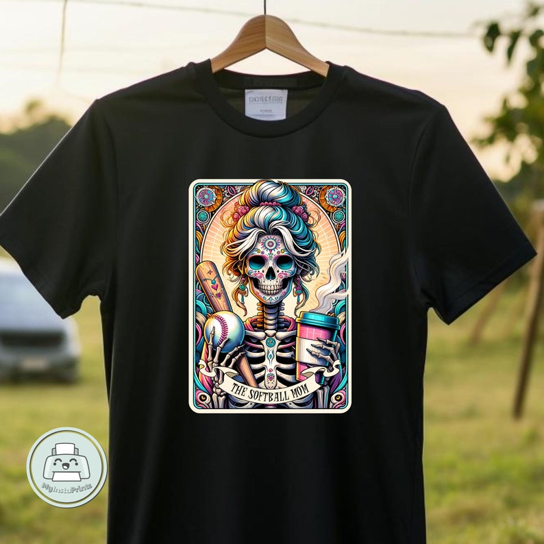 May include: Black t-shirt with a colorful illustration of a sugar skull woman holding a baseball bat and a coffee cup. The text "The Softball Mom" is below the image.