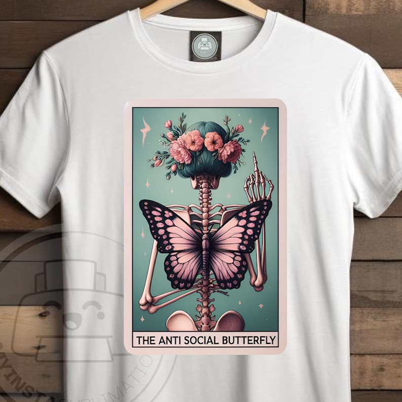 K&ouml;nnte beinhalten: Ein wei&szlig;es T-Shirt mit einem grafischen Aufdruck eines Skeletts mit einem Schmetterling auf dem R&uuml;cken. Das Skelett tr&auml;gt eine Blumenkrone und zeigt den Mittelfinger. Der Text "The Anti Social Butterfly" ist unter dem Grafikdruck aufgedruckt.