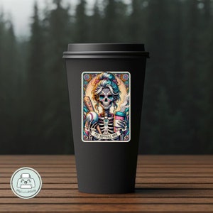 May include: A black coffee mug with a colorful sticker featuring a sugar skull woman holding a baseball bat and a coffee cup. The sticker says "The Softball Mom".