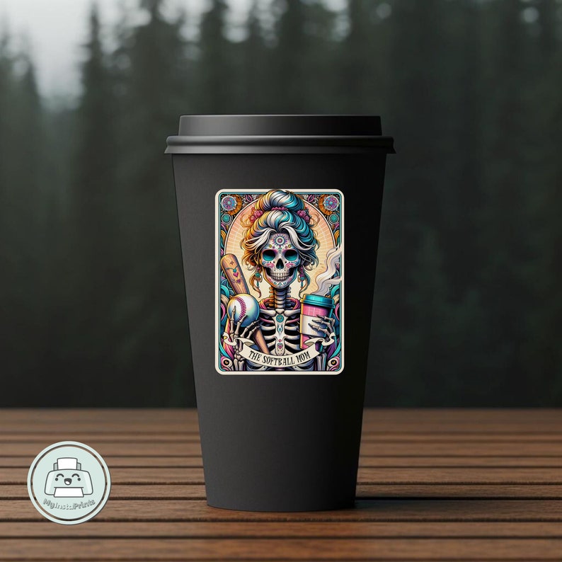 May include: A black coffee mug with a colorful sticker featuring a sugar skull woman holding a baseball bat and a coffee cup. The sticker says "The Softball Mom".