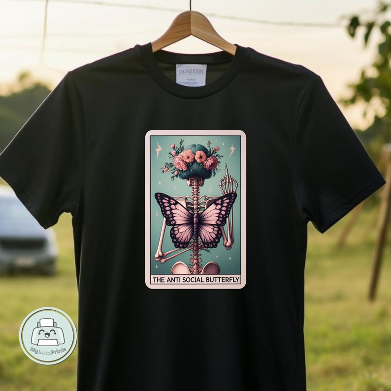 K&ouml;nnte beinhalten: Schwarzes T-Shirt mit einem Grafikdruck eines Skeletts mit einem Schmetterling auf dem R&uuml;cken. Das Skelett tr&auml;gt eine Blumenkrone und zeigt den Mittelfinger. Der Text "The Anti Social Butterfly" befindet sich unter dem Grafikdruck.